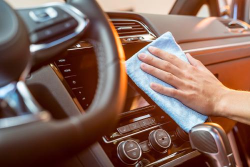 Eine Hand mit Lappen wischt über eine Mittelkonsole in einem Auto